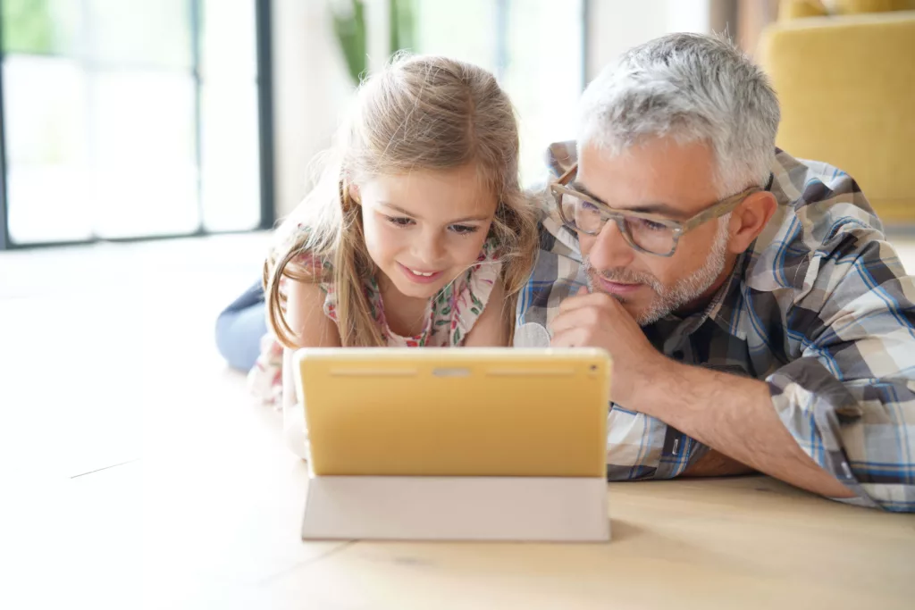 older man with hearing aid browses computer with grandkid