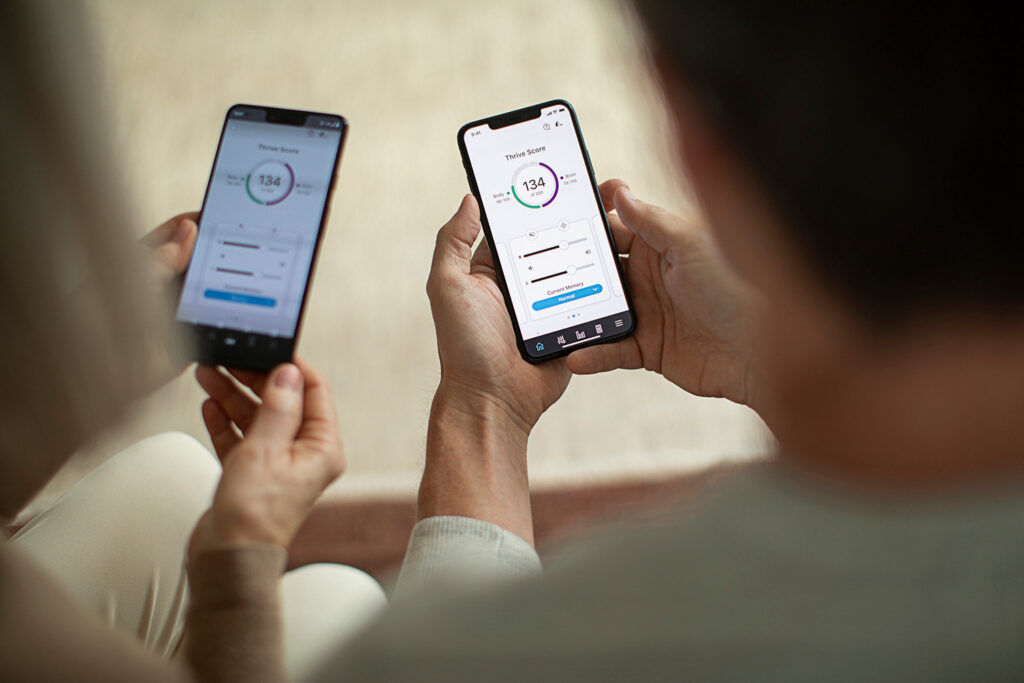 2 individuals seated on a couch compare their thrive care app scores on their smartphones