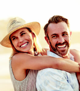 woman hugs man from behind while both smile and look off into the distance
