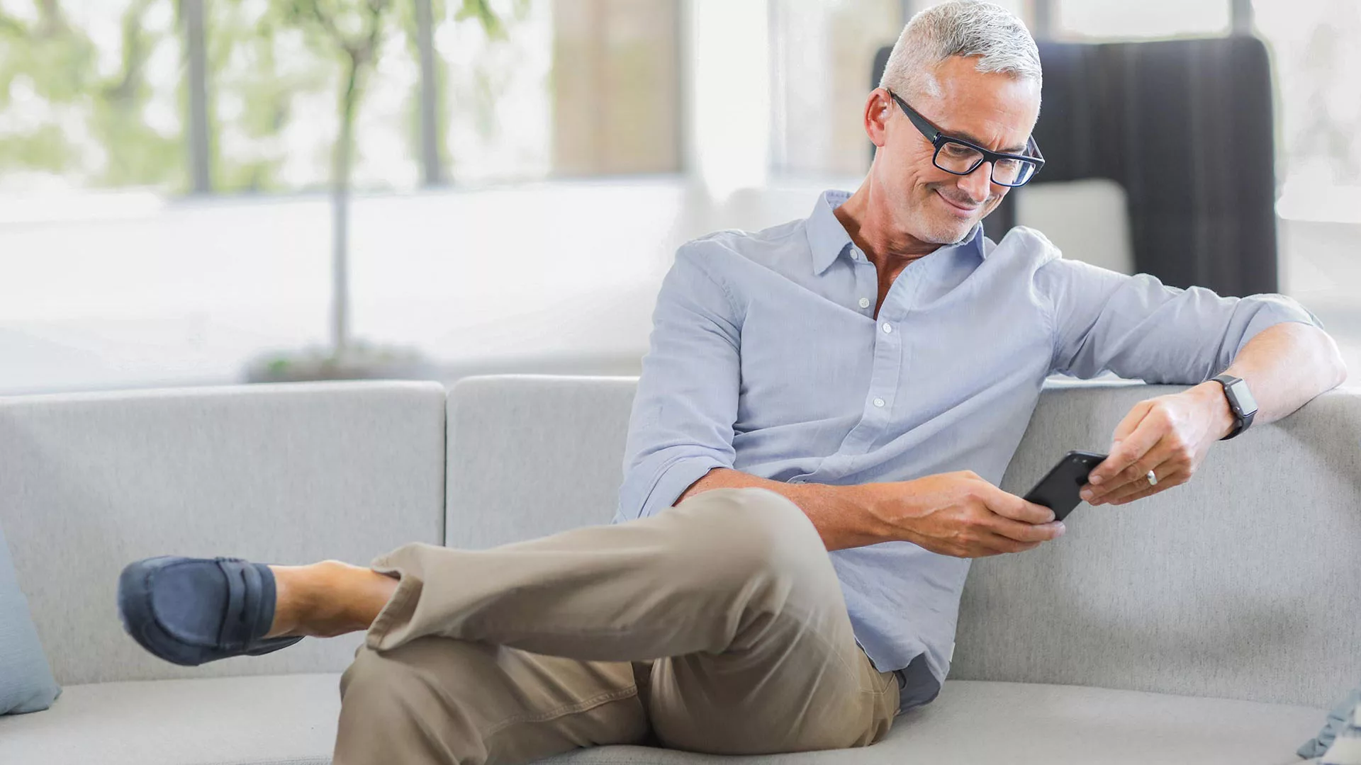 Man sitting on couch looking at ihear on smartphone
