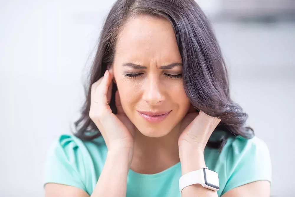 woman covers her ears to drown out the irritation caused by her tinnitus