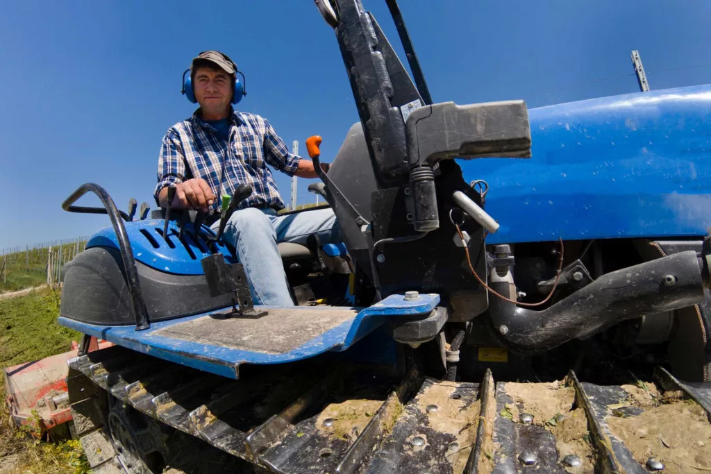 Farmer riding a crawler tractor while wearing noise-free headphones to protect his hearing